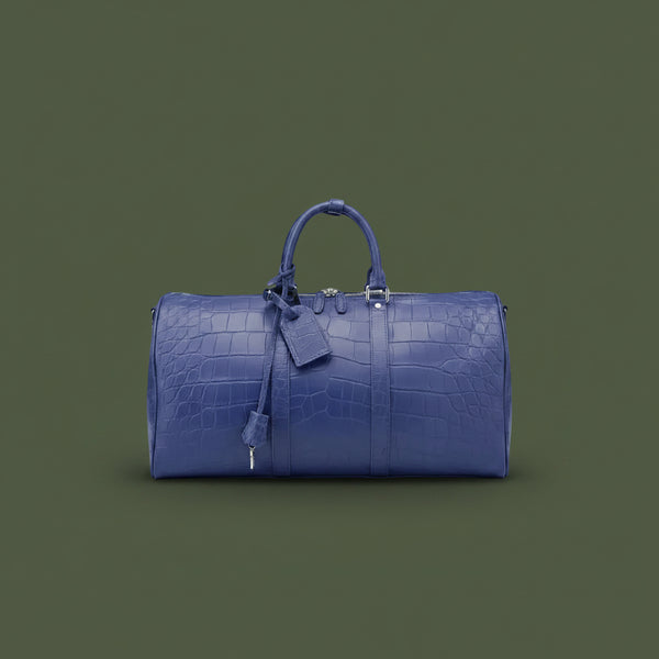 Blue leather duffel bag with crocodile texture on a dark green background
