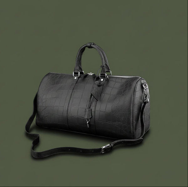 Black leather duffel bag with crocodile texture on a black background